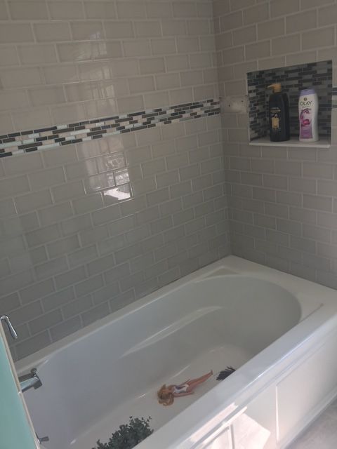 A bathroom with a white bathtub and gray tile walls, including a decorative mosaic border and built-in shelf.