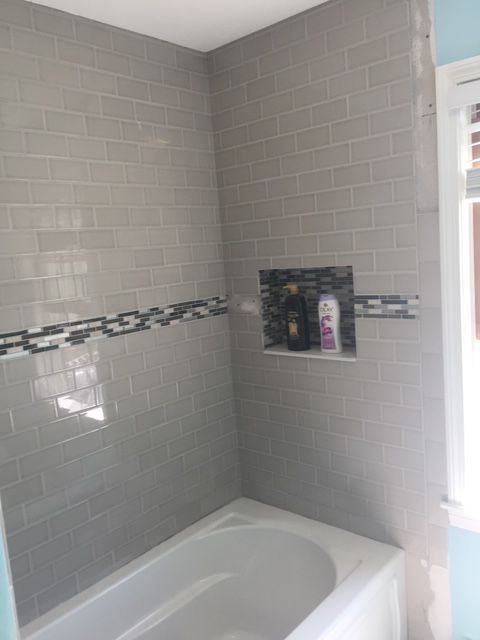 Gray tiled shower with a decorative border and built-in shelf, adjacent to a window.
