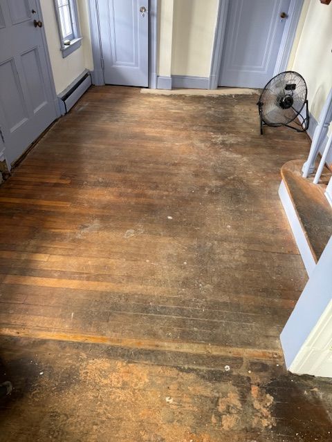 Wooden floor needing refinishing; visible dirt, dark stains, and debris. Blue doors and baseboards.