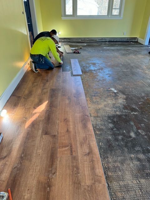 Two people installing wood-look flooring in a room with yellow walls.