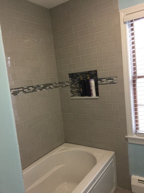 Gray tiled bathroom shower wall above a white bathtub with a built-in shelf.