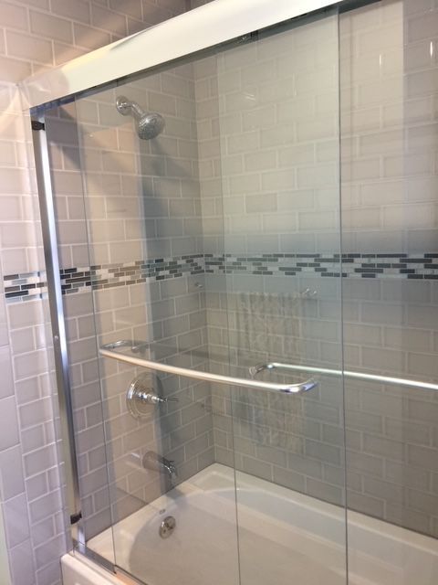 Shower stall with sliding glass doors, chrome hardware, light gray tiled walls, and a white bathtub.