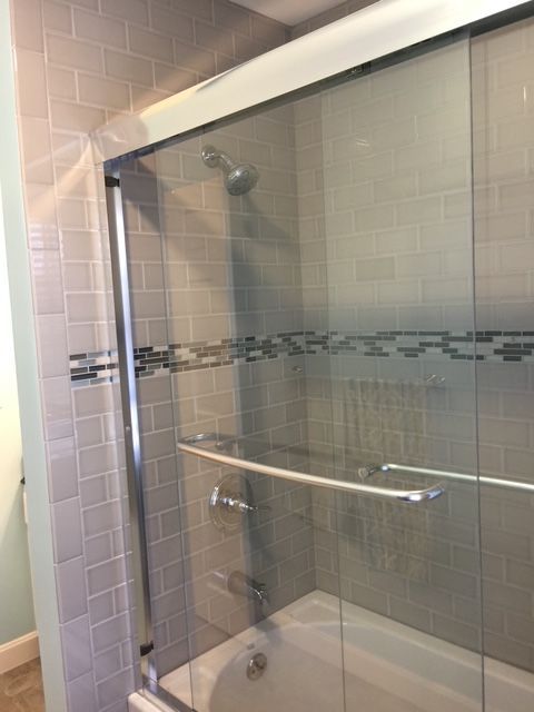 Shower with glass sliding doors, gray tiled walls, and a bathtub.