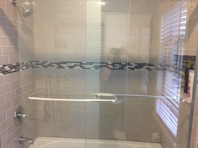 Shower stall with glass doors, gray tiled walls, decorative mosaic border.