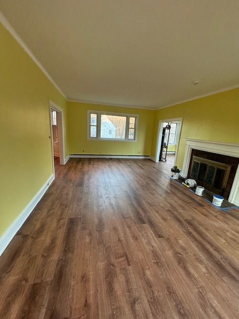Yellow-painted room with wood-look flooring, fireplace, and window. Empty interior with white trim.