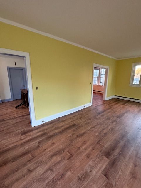 Empty room with yellow walls, white trim, and brown wood-look flooring. Two doorways and a window are visible.