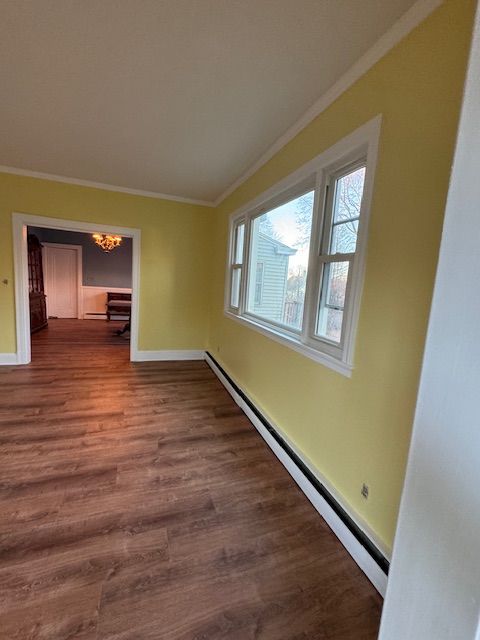 Yellow-walled room with a window, white trim, and wood-look flooring; an archway leads to another room.