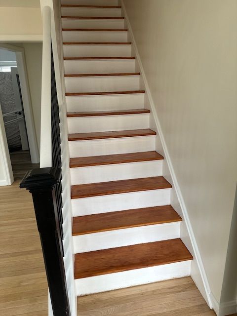 Staircase with wooden steps and white risers, black banister on the left, cream-colored walls.