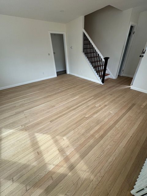 Light wood floors in an empty room, a staircase with black railing, white walls, and two open doorways.