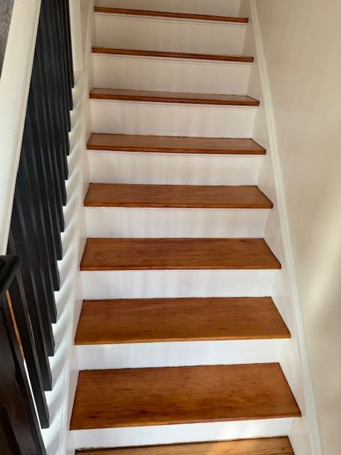 Wooden staircase with white risers and black railing.