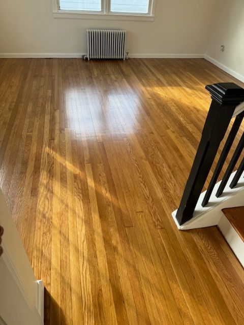 Hardwood floor in a room, with sunlight, a radiator, and part of a staircase.