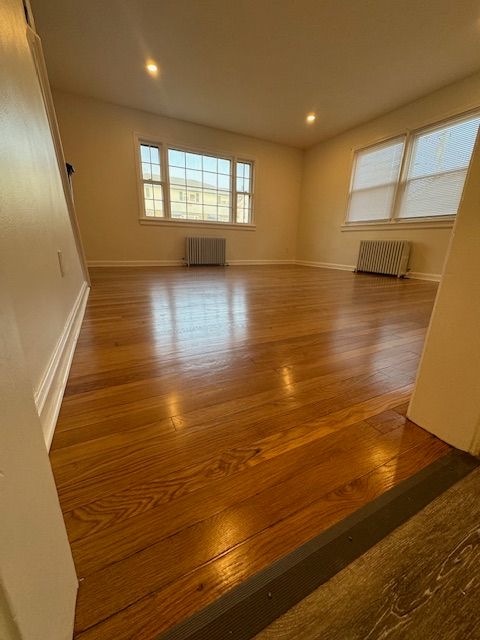 Hardwood floor in a room with two windows, radiators, and white walls.