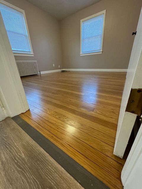 Empty room with hardwood floors, two windows, and radiator.