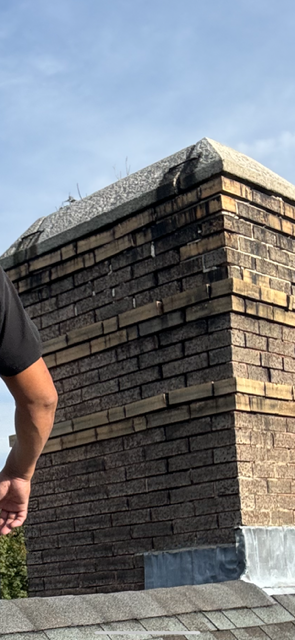 Brick chimney on a roof, part of a person in frame. Sky visible in the background.