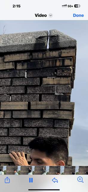 A man peeking from behind a brick wall, possibly a chimney.