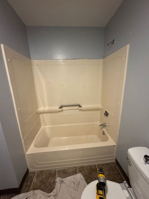 A beige bathtub and surround in a bathroom with blue walls and a toilet.