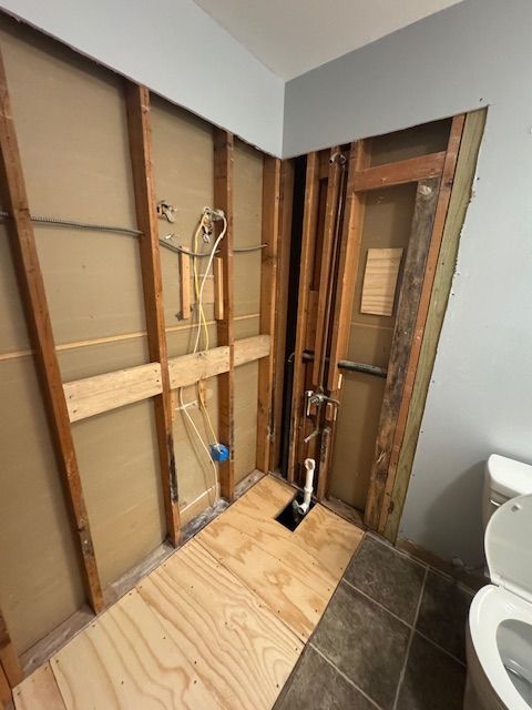 Bathroom under construction, exposed studs, pipes, unfinished flooring, and toilet.