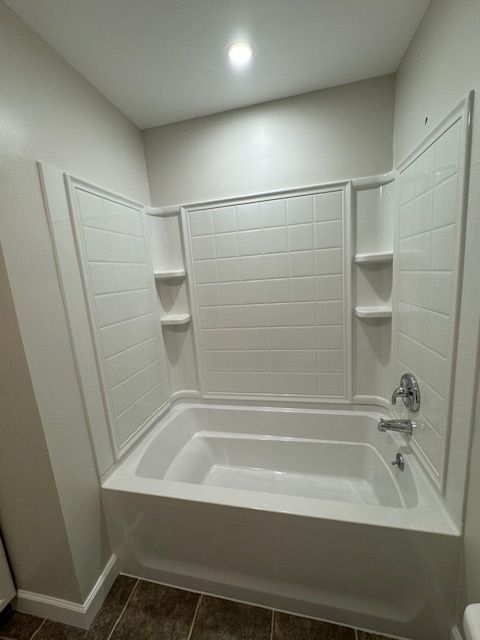 White bathroom with a tub and shower surround, shelves, and chrome fixtures.