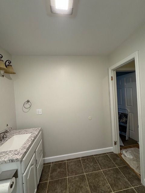 Bathroom with a white vanity, brown floor tiles, and a doorway to another room.