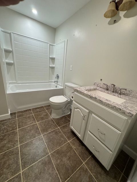 Bathroom with white tub/shower, toilet, vanity, and brown tile floor. Beige walls.