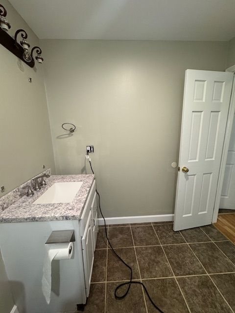 Bathroom with a sink and countertop, brown tile floor, and a white door. Wall is painted light green.