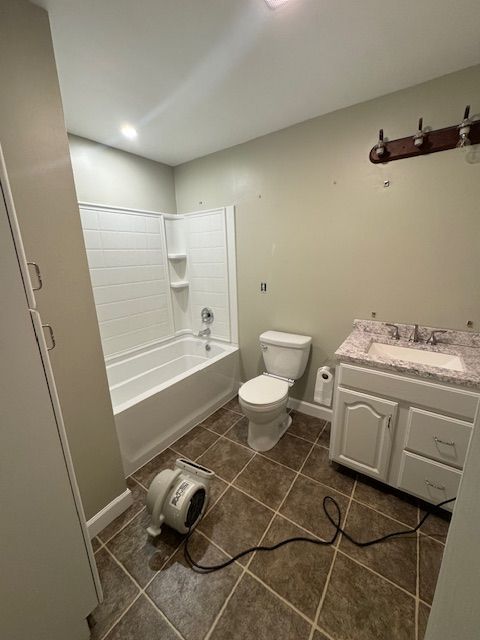 Bathroom with a white bathtub and toilet, brown tile floor, and a white vanity.