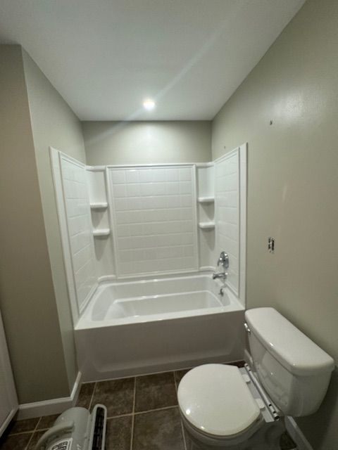 Bathroom with white bathtub, toilet, and beige walls, brown tile floor.