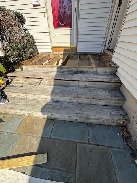 Wooden porch stairs under construction, leading to a front door with missing boards.