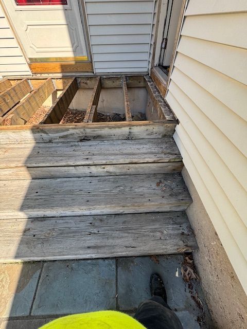 Wooden steps leading to a house. Stair treads are weathered. The top landing shows exposed framing.
