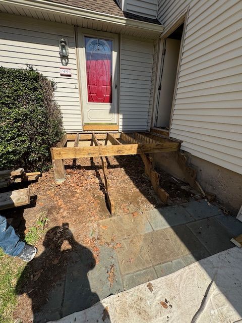 Damaged wooden porch and steps leading to a front door with a red paneled door.