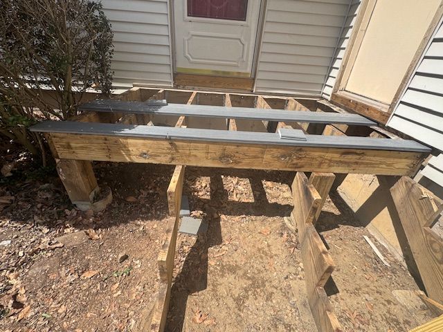 A partially built wooden porch in front of a house. The frame is constructed with exposed beams and support posts.