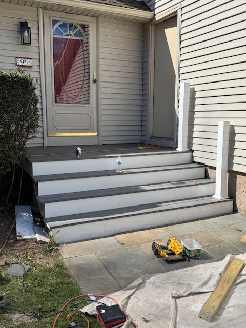 Exterior view of gray stairs leading to a front door, with white railing posts. Construction tools visible.