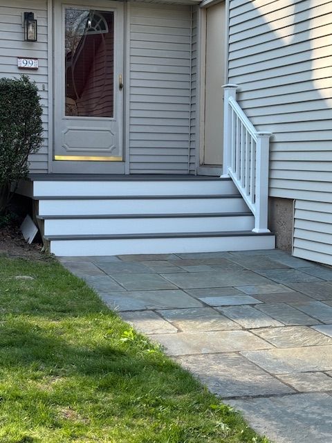 Front steps to a house with white railing and gray siding, stone walkway in front.