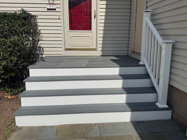 Grey and white outdoor steps leading up to a front door with a white railing.
