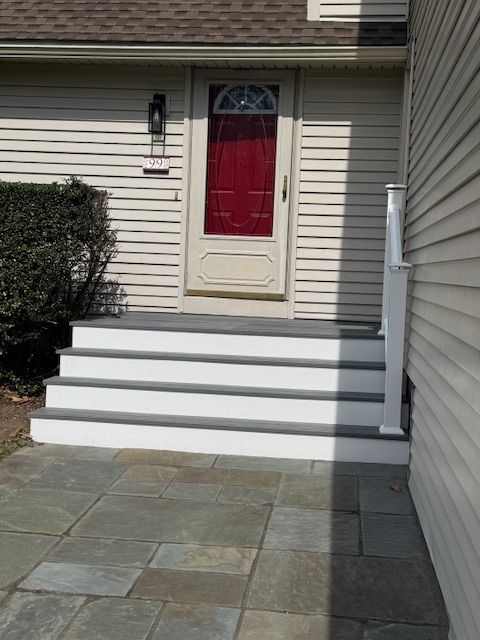 Exterior view of a house with a red door, white steps with gray trim, and a stone patio.