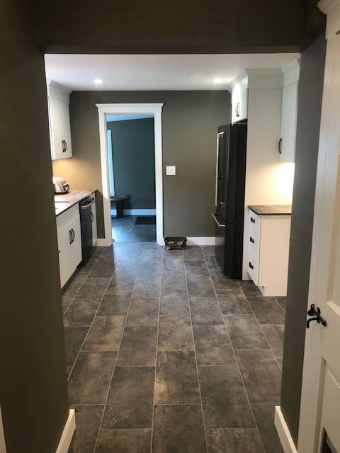 Kitchen with white cabinets, gray tile floor, dark green walls, and black refrigerator.