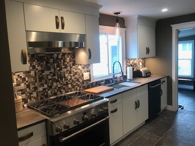 Modern kitchen with white cabinets, dark countertops, and a mosaic backsplash.