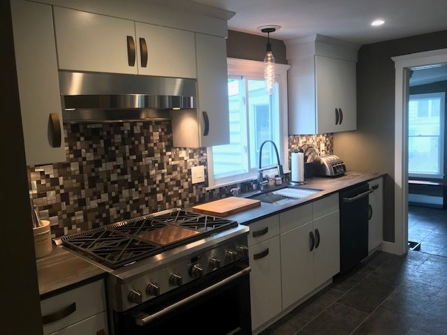 Kitchen with white cabinets, dark countertops, tile backsplash, and stainless steel appliances.