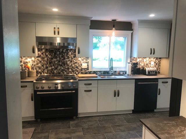 Modern kitchen with light gray cabinets, dark countertops, dark tiled floor, and stainless steel oven.
