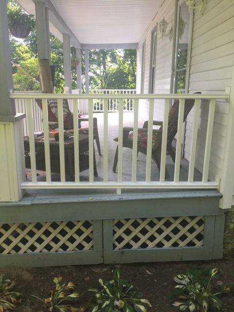 White porch with railing and latticework, chairs visible through the railing, exterior view.