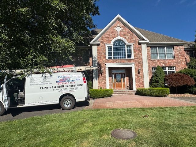 White van with logo parked in front of a brick house; sunny day.