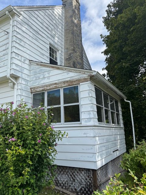 White house exterior with porch and chimney, cloudy sky.