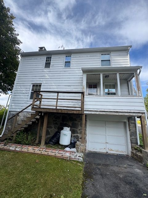 Back of a two-story white house with a deck, screened porch, and garage. Propane tank visible. Cloudy sky.