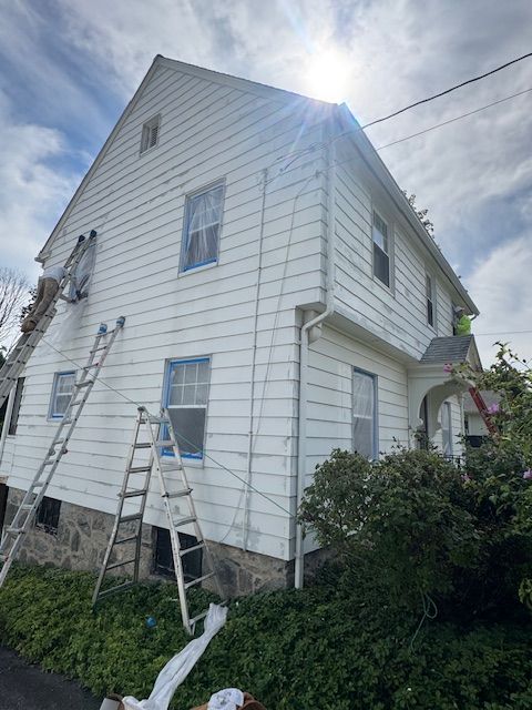 House exterior being painted white with ladders. Workers visible.