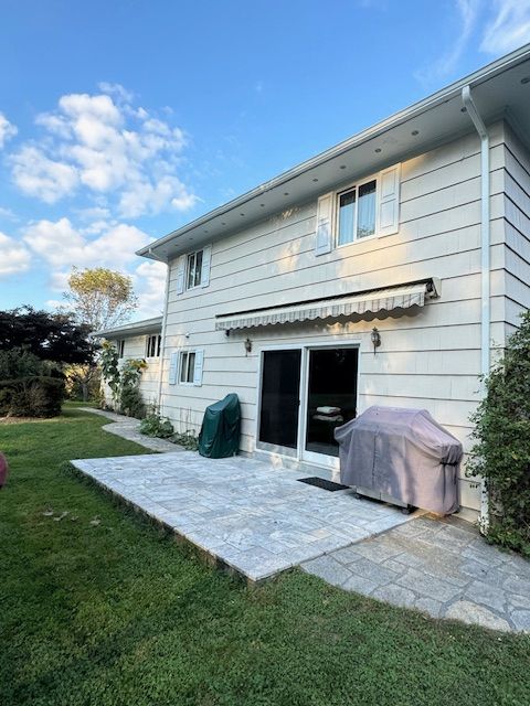 Two-story house with a patio, awning, and covered grill. Green lawn, blue sky, and white siding.