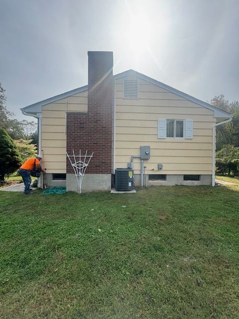 Person working on the side of a yellow house with a brick chimney and an air conditioning unit.