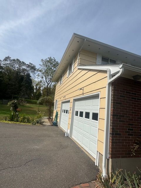 Two-story house with yellow siding and white garage doors, set against a green lawn and blue sky.