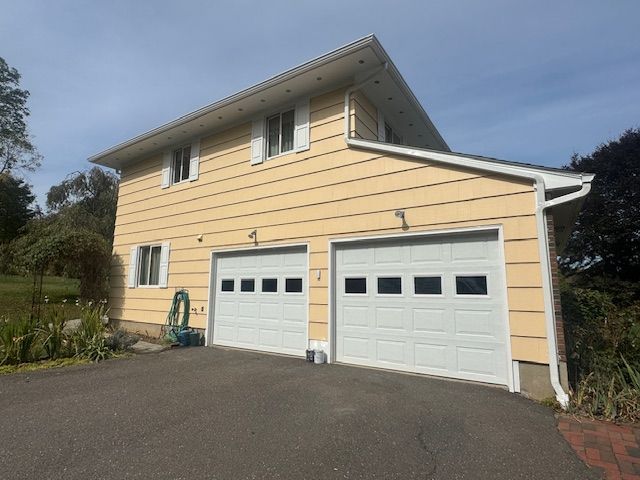 Yellow two-story house with white garage doors and shutters, set on a driveway.