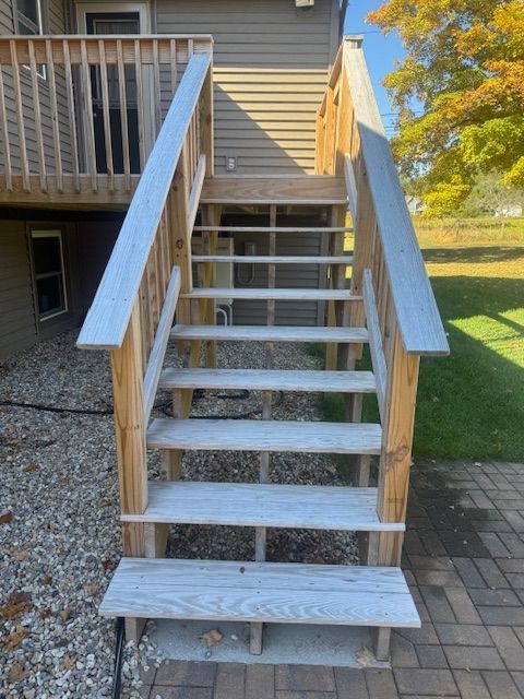Wooden outdoor stairs leading from a deck to a brick patio, with wooden handrails.