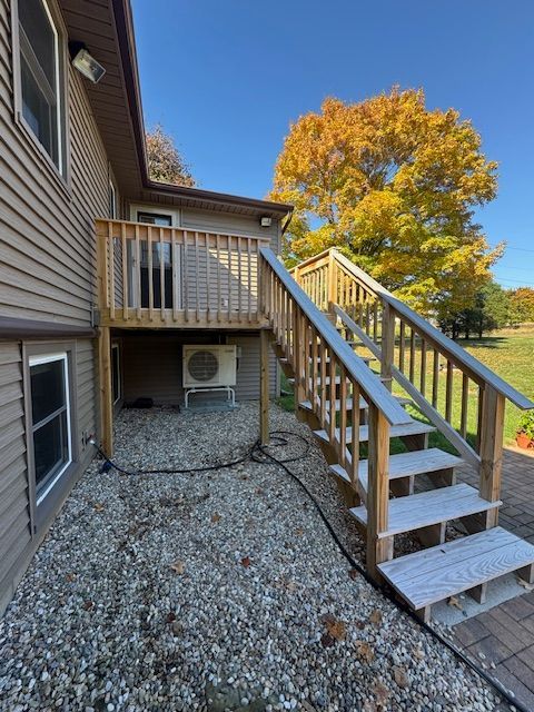 Exterior view of a two-level wooden deck with stairs. A unit is installed under the deck, and gravel covers the ground.